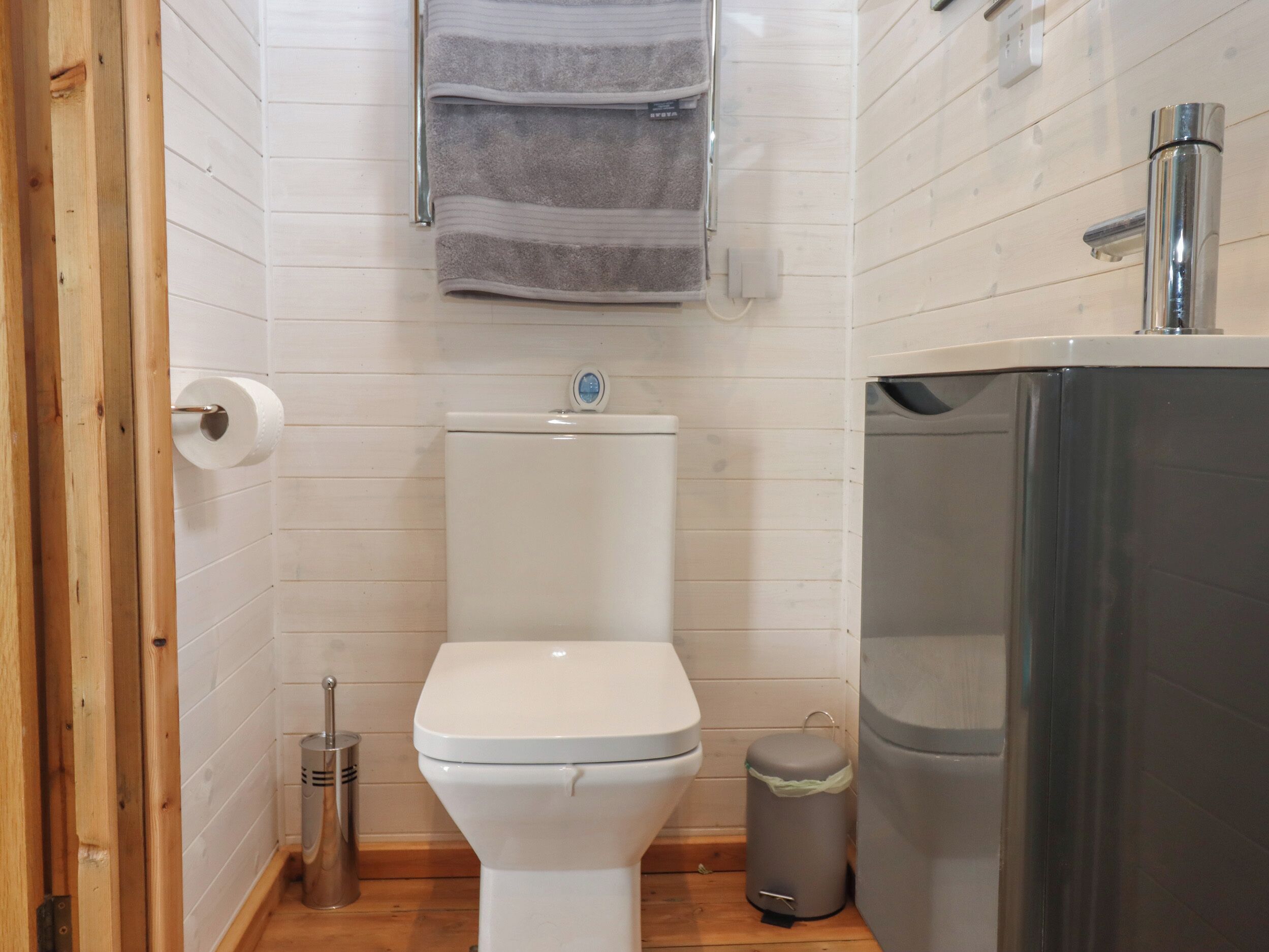 A small bathroom with a toilet, a trash bin, and a towel rack.