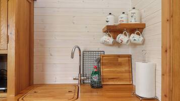 A wooden kitchen with a sink, faucet, and a shelf holding mugs.