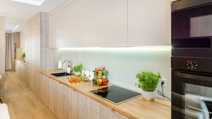 A modern kitchen with wooden cabinets, a black countertop, a built-in oven, and a small potted plant. - Lumina glamour 3 bedroom apartment (Lodz)