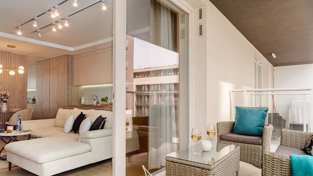 A modern living room with a sofa, wicker furniture, and a glass door leading to a balcony. - Lumina glamour 3 bedroom apartment (Lodz)