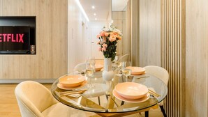 A modern dining area with a glass table, peach-colored plates, and a vase of flowers. - Lumina glamour 3 bedroom apartment (Lodz)