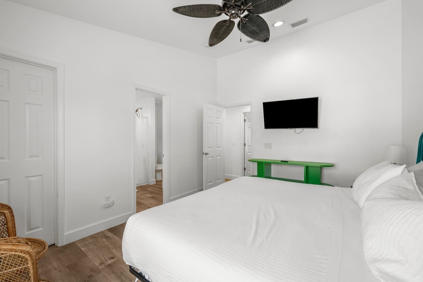 A bedroom with a large bed, a green bench, a flat-screen TV, and a ceiling fan.