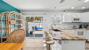 Cocina moderna con armarios blancos, encimera de granito y vista a un patio trasero con piscina y sillones de descanso.