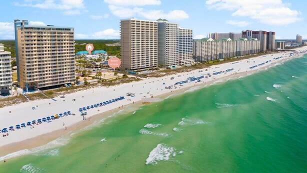 Un hotel costero con varios edificios altos, una playa con sombrillas y una vista despejada del océano.
