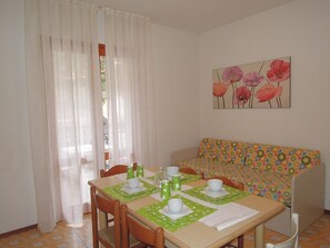 Un comedor con una mesa dispuesta para cuatro, sillas, un sofá y un cuadro de flores en la pared.