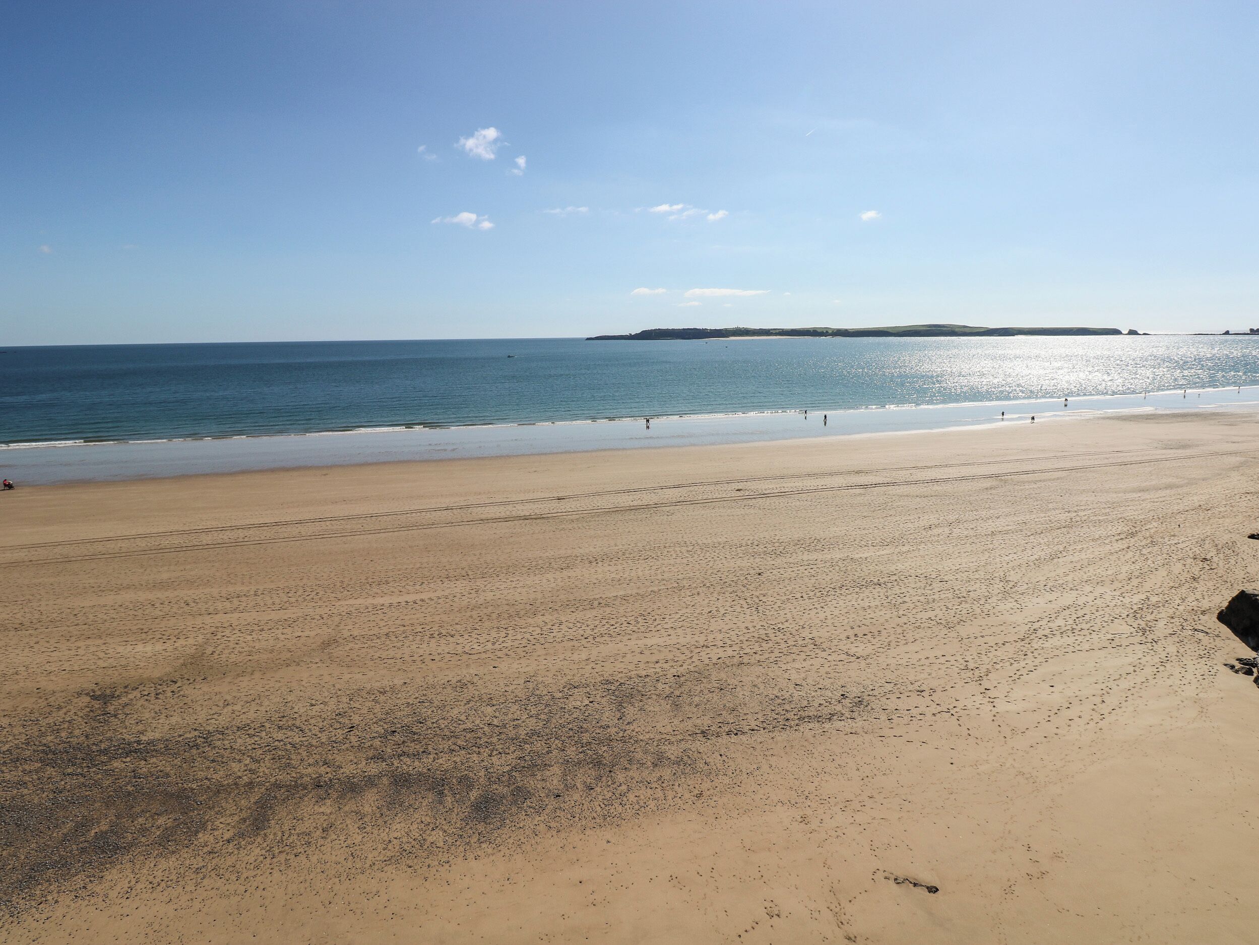 A wide sandy beach with a clear sky and calm sea.