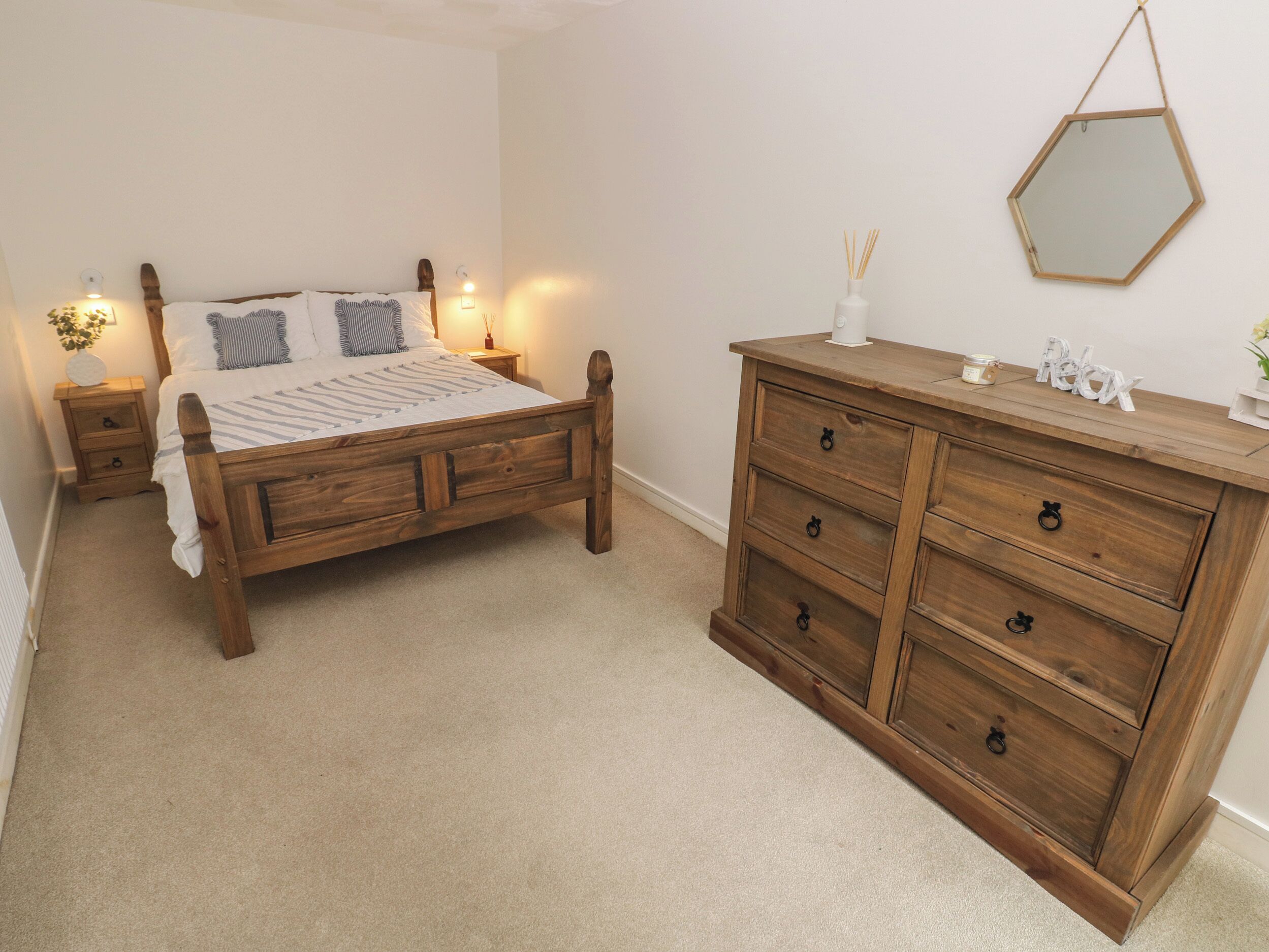 A bedroom with a wooden bed, a wooden dresser, and a nightstand with a lamp.