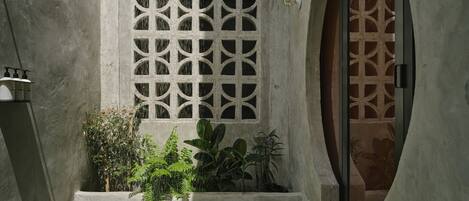 Une cour agrémentée d’un élément aquatique, un mur en béton orné d’un motif géométrique et une porte en bois.