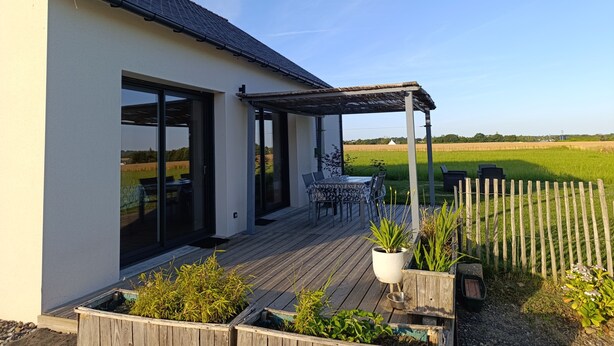 A modern house with a patio, large windows, and a view of a green field. - Maison Neuve de Plain-pied (Pipriac)
