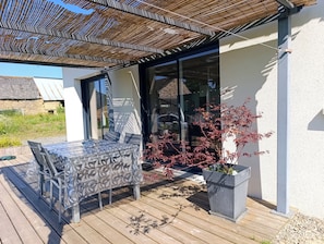 Un patio al aire libre con una mesa, sillas, una pérgola y una planta en maceta.