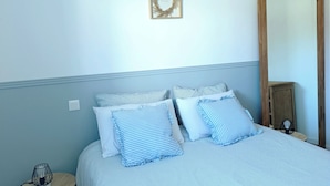 A bedroom with a bed, bedside table, lamp, and a mirror. - Maison Neuve de Plain-pied (Pipriac)