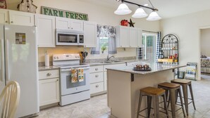 A modern kitchen with white cabinetry, a central island with stools, a microwave, an oven, and a refrigerator. - Charming Gravois Mills Escape w/ Private Backyard! (Gravois Mills)