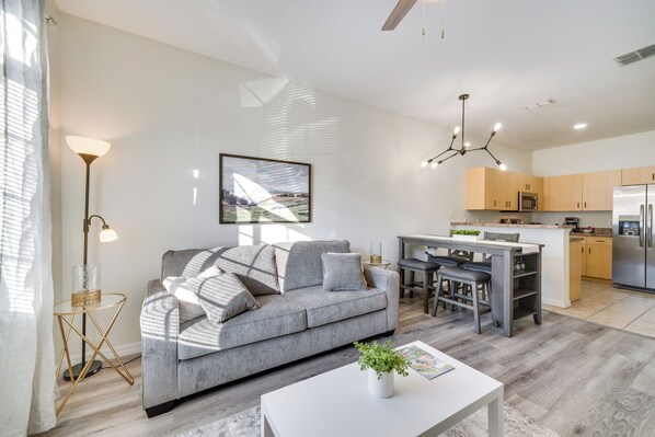 A modern living room with a grey sofa, a coffee table with a plant, and a dining area with a table and chairs. - Community Pool: Family-Friendly Florida Condo! (Poinciana)