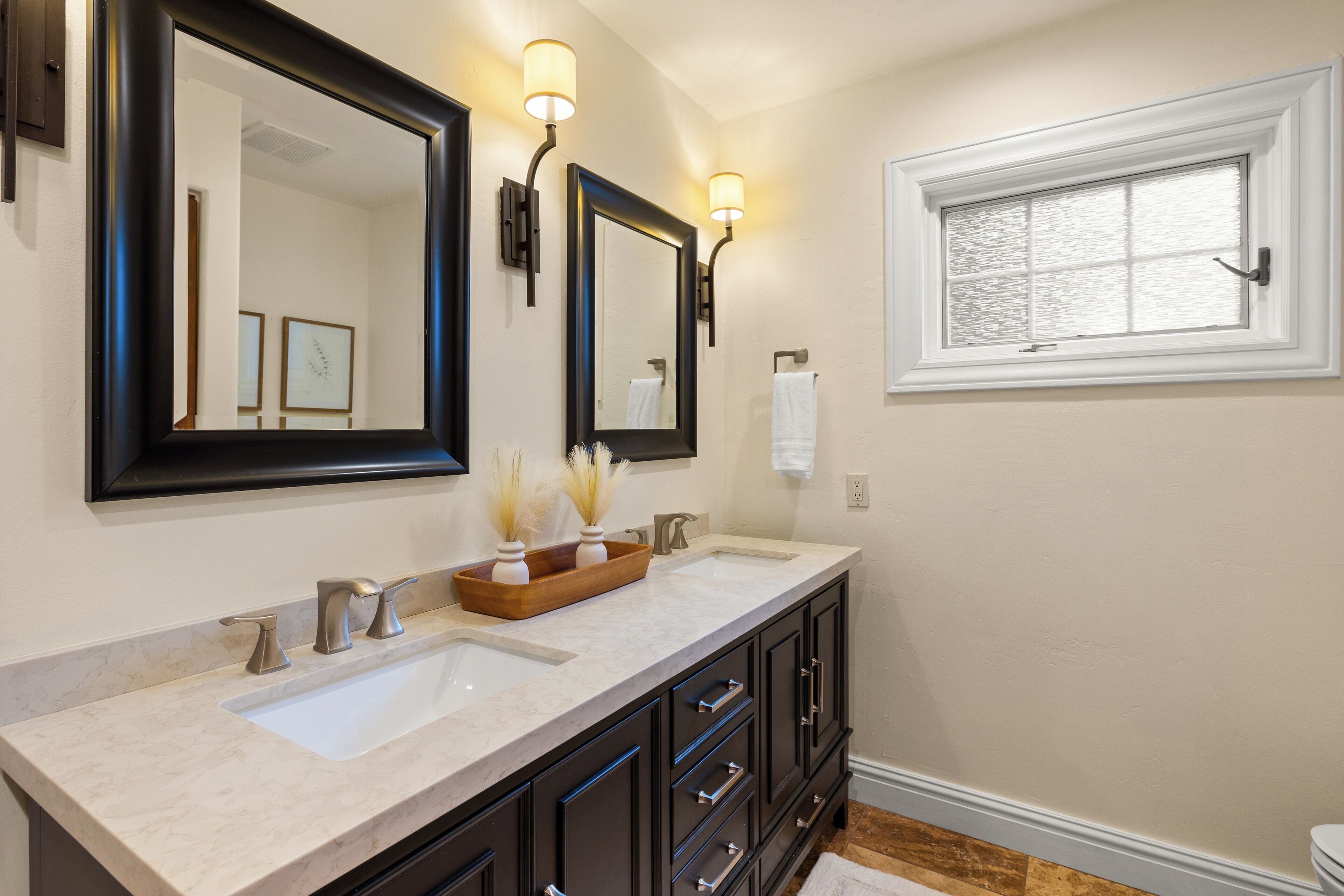 A bathroom with a double sink vanity, two wall-mounted mirrors, and a window with frosted glass.