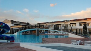 Une piscine avec un pont, des chaises longues et un bâtiment moderne doté d’un toit en tuiles.