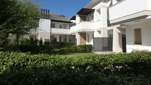 Un immeuble résidentiel moderne à plusieurs étages, doté d’un jardin bien entretenu et surplombant un ciel d’un bleu éclatant.