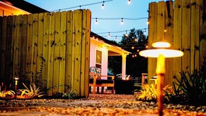 A wooden fence enclosure with string lights, a bench, and a fire pit.