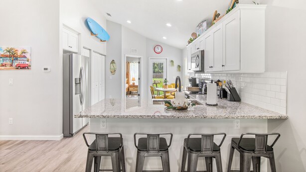 A modern kitchen with white cabinets, a granite countertop, and three bar stools.