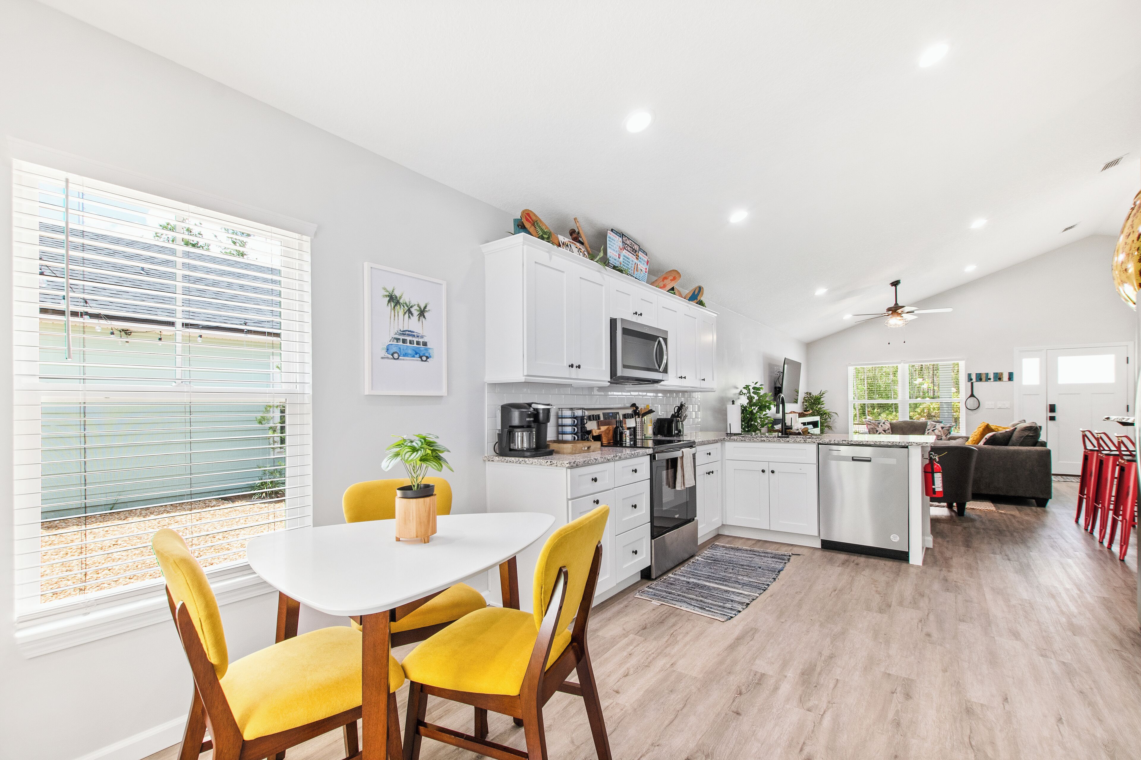Een moderne keuken met witte kasten, een centraal eiland en een eetgedeelte met gele stoelen.