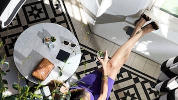 A person seated at a round table with a small plant, a wallet, and sunglasses on it.