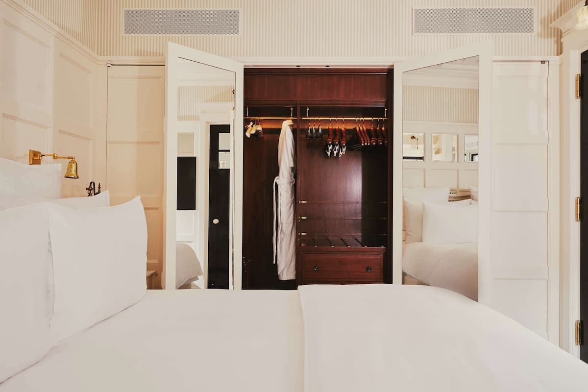 A hotel room with a large bed, a wardrobe with hanging clothes, and a bathroom with a bathtub and a toilet.