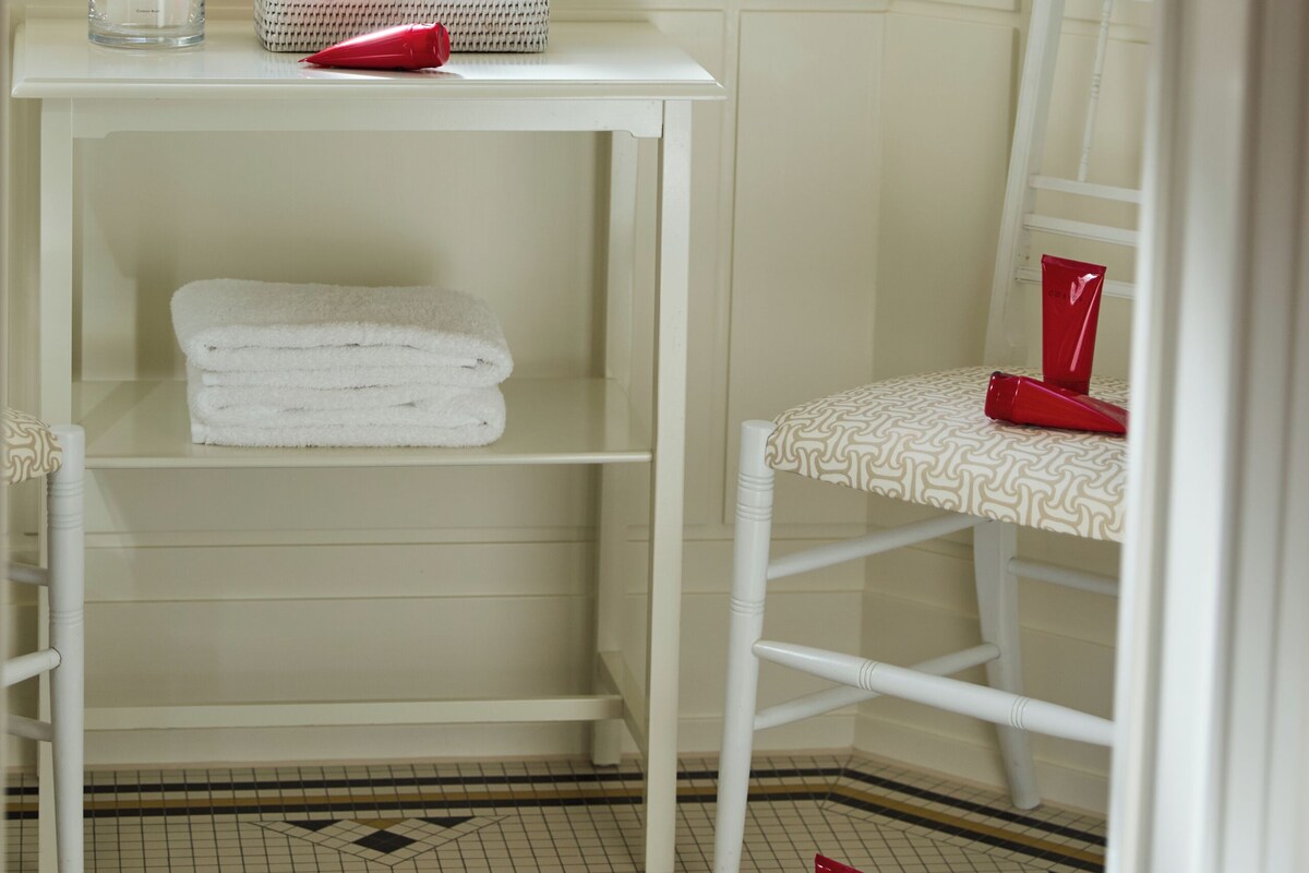 A bathroom with a white vanity, a window with a green view, and a white chair.