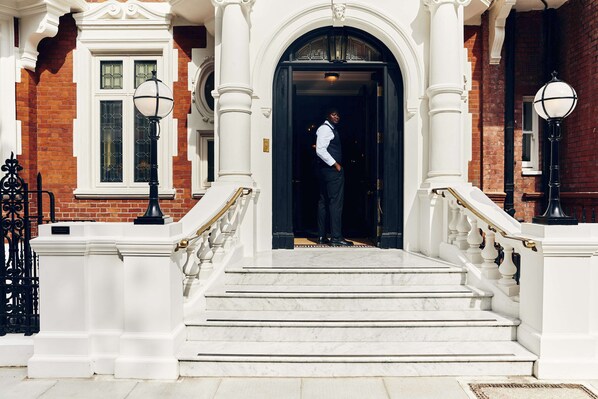 A grand entrance with marble steps, a black and white color scheme, and a person standing at the doorway. - At Sloane (London)