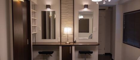 A hotel room with a bed, a desk with two bar stools, a mirror, a lamp, and a chandelier.