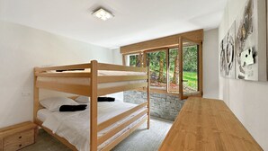 Habitación con literas, una mesa de madera, pared de piedra y ventana con vista al bosque.
