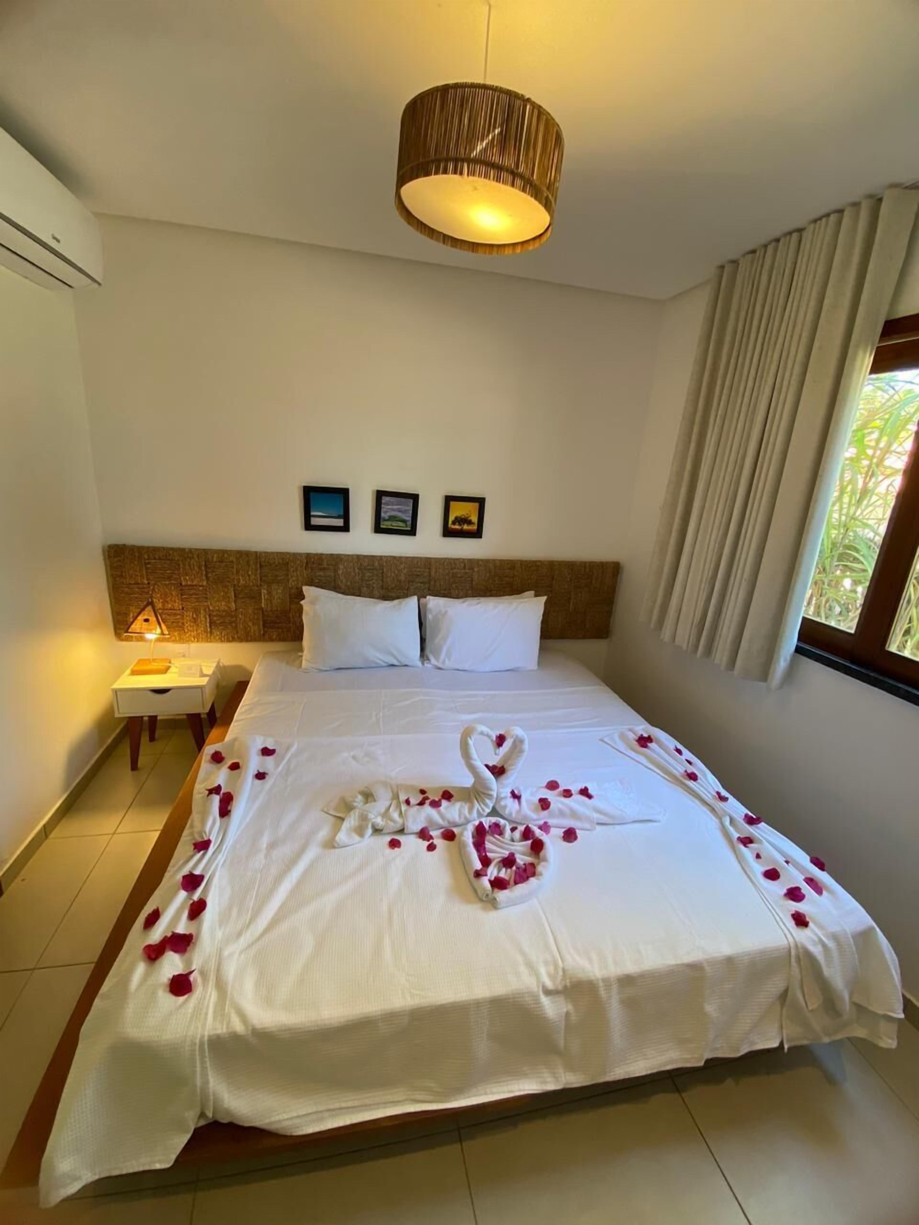 Una habitación de hotel con cama, mesita de noche, lámpara, aire acondicionado instalado en la pared y ventana con cortinas.