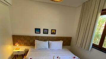 Una habitación de hotel con cama, mesita de noche, lámpara, aire acondicionado instalado en la pared y ventana con cortinas.