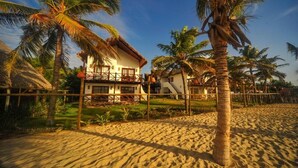 A beachfront property with a thatched-roof house, palm trees, and a sandy beach.