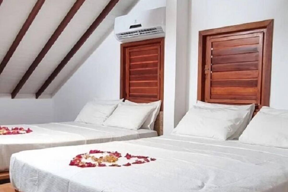 A hotel room with two beds, wooden headboards, white bedding, and an air conditioning unit on the wall.