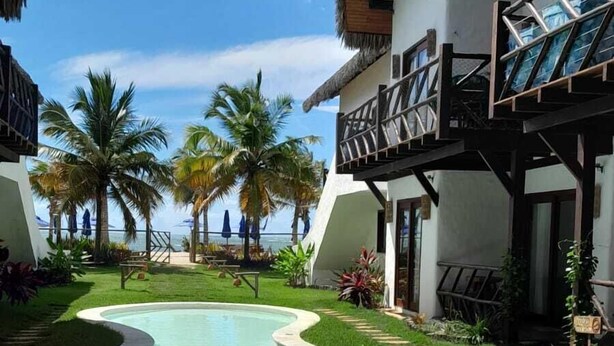 A resort with a central swimming pool, palm trees, and a view of the ocean.