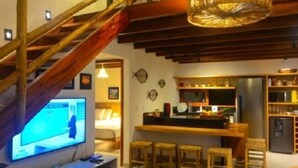 A modern interior with a wooden staircase, a kitchen area with bar stools, and a television on a white cabinet.