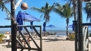 A beach entrance with a wooden gate, palm trees, and blue umbrellas.