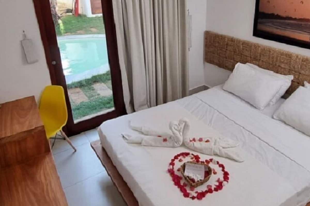 A hotel room with a bed, a wooden desk, a yellow chair, and a view of a swimming pool through the door.