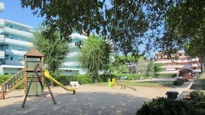 A playground with a slide and swings, surrounded by trees and buildings. - Homely Apartment With Shared Pools - Beahost (San Michele al Tagliamento)