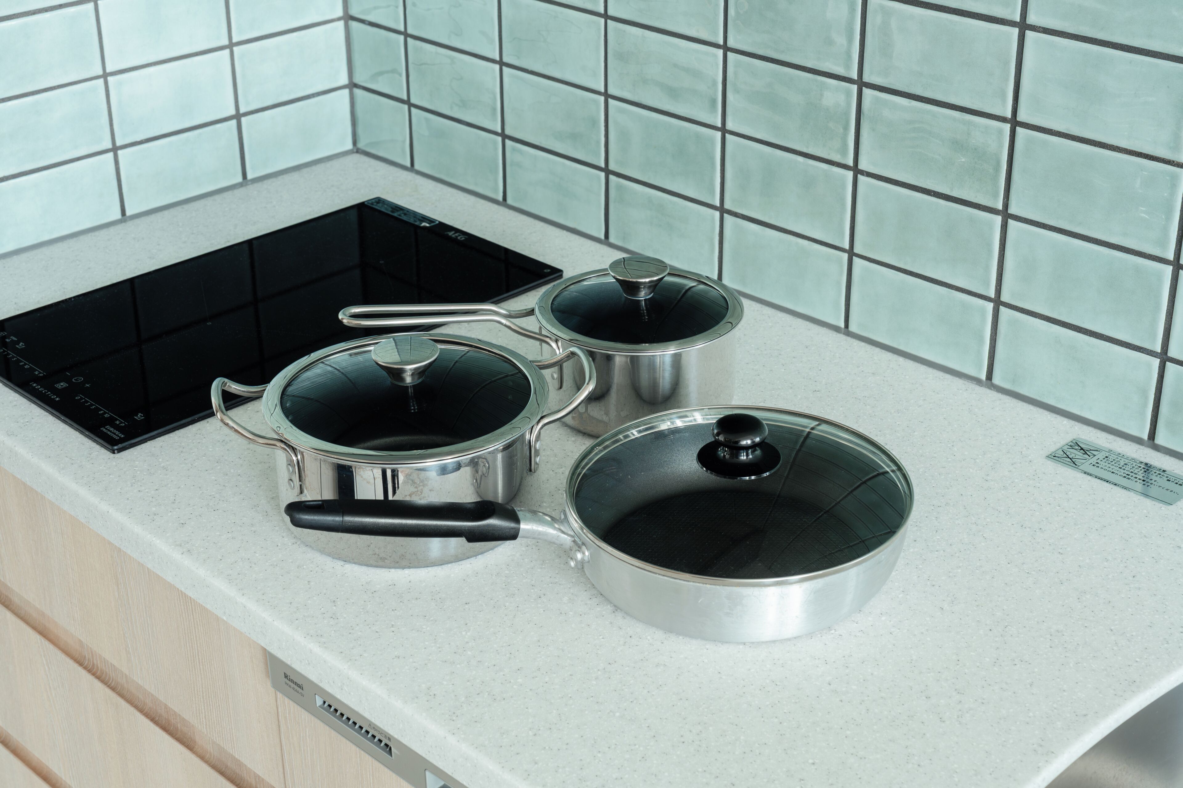A kitchen with a modern induction cooktop, stainless steel pots, and a glass lid on the counter.