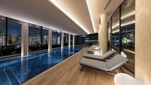 A modern indoor swimming pool with lounge chairs, large windows, and a city view at night. - Hyatt House Tokyo Shibuya (Tokyo)
