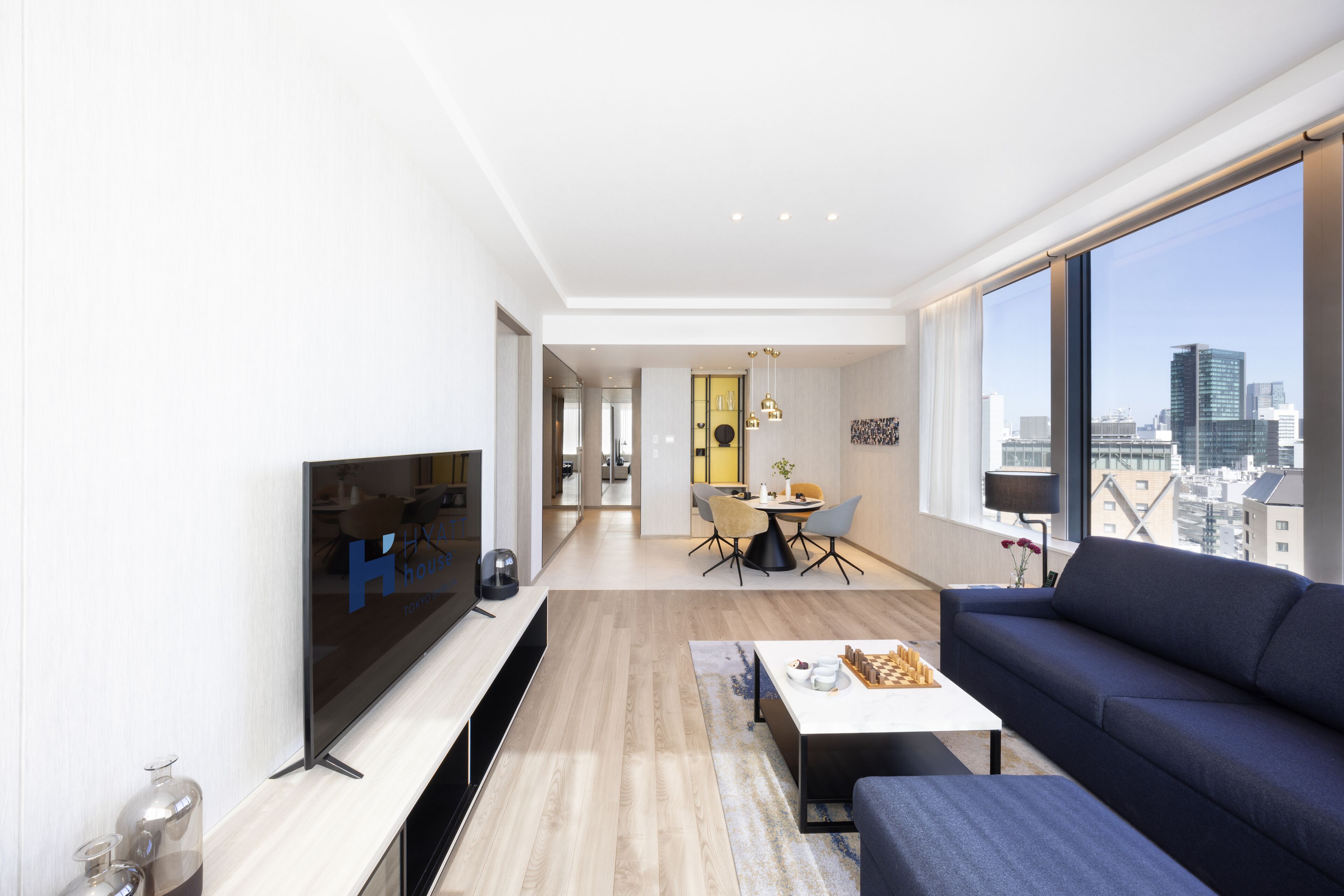 A modern living room with a large TV, a sofa, and a dining area with chairs and a table.