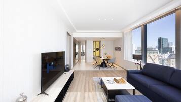 A modern living room with a large TV, a sofa, and a dining area with chairs and a table.