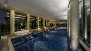 Une piscine intérieure au design moderne, dotée d’un large espace au bord du bassin avec des chaises longues et un jacuzzi.