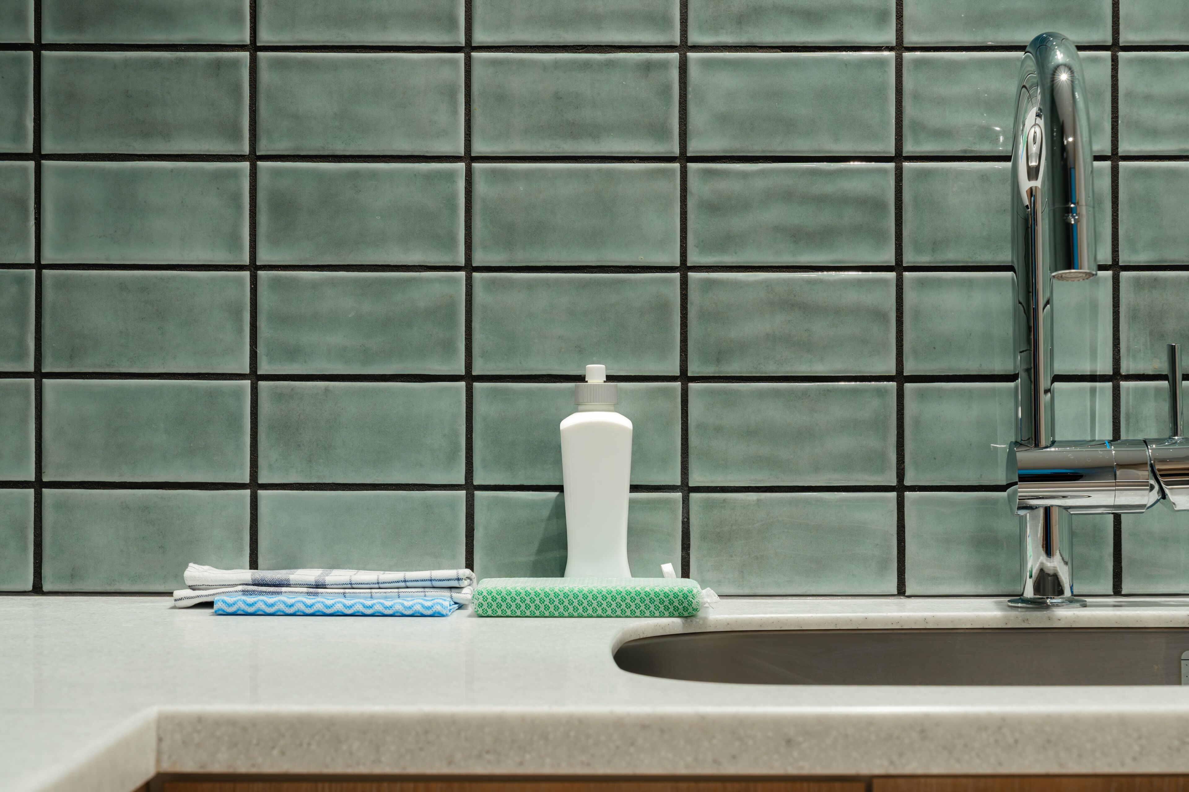A kitchen with a tiled backsplash, a sink, a faucet, a bottle, and a cloth.