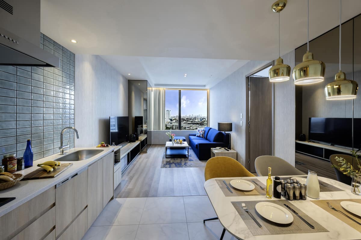 A modern kitchen with a large window, a dining area with a table set for two, and a living area with a sofa and a TV.