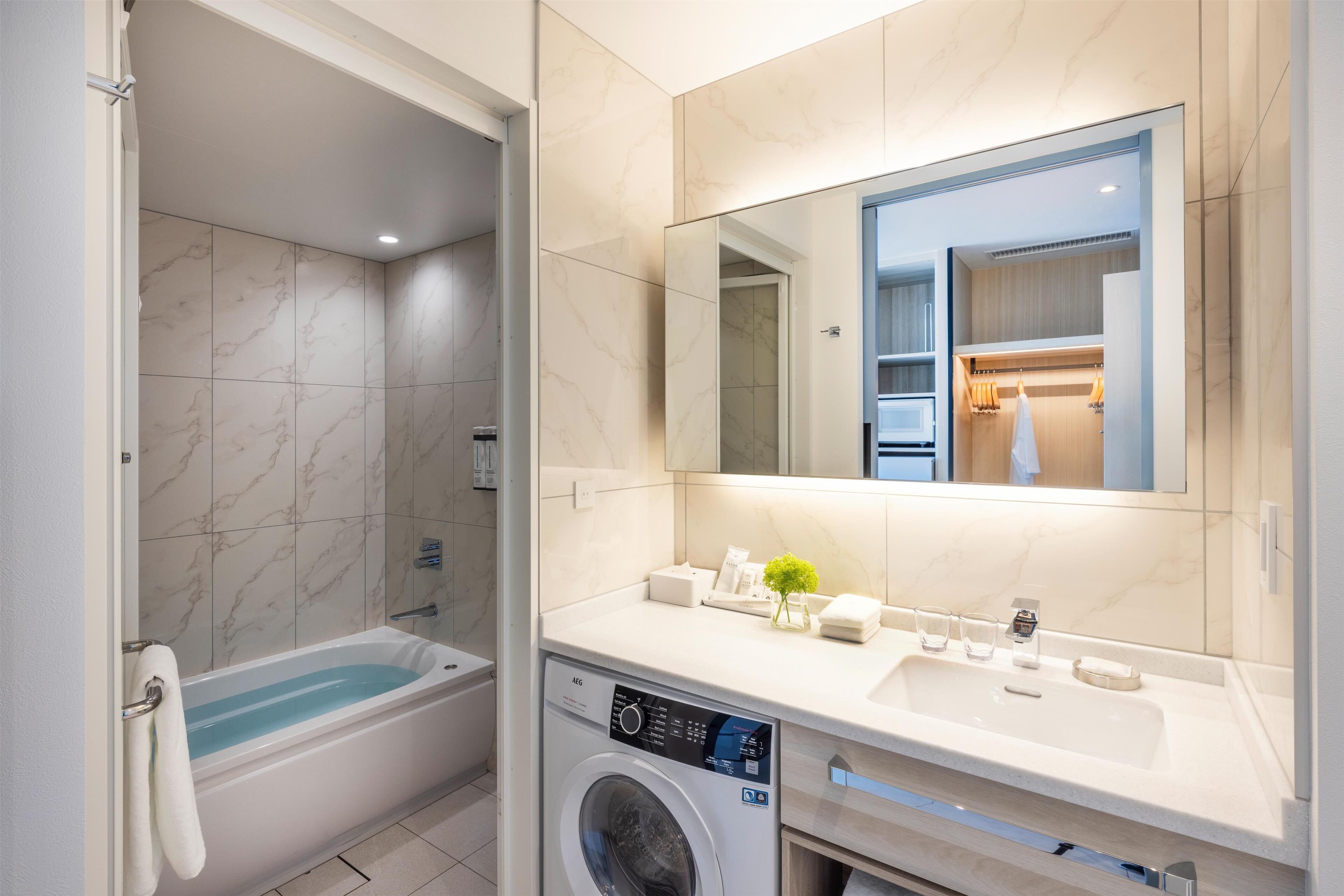 A modern bathroom with a bathtub, a washing machine, a sink, and a large mirror.