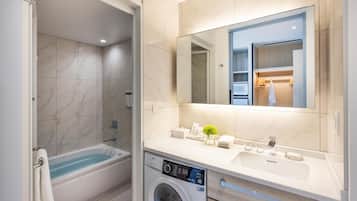 A modern bathroom with a bathtub, a washing machine, a sink, and a large mirror.