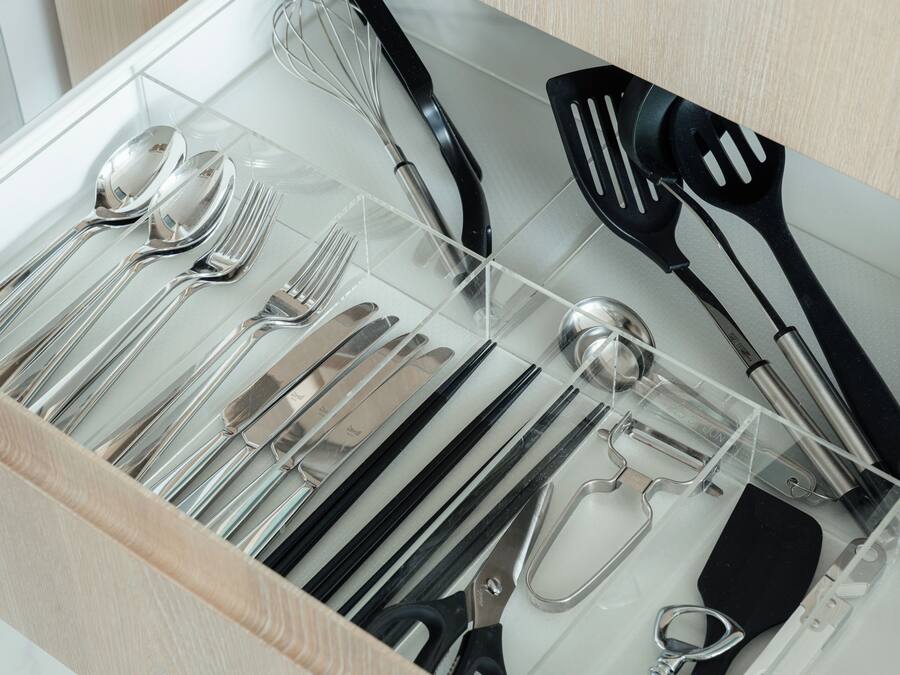 A drawer with kitchen utensils including spoons, forks, knives, a whisk, spatulas, and scissors.