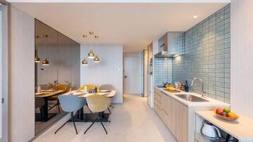 A modern kitchen with a dining area, featuring a large island, pendant lights, and a tiled backsplash.