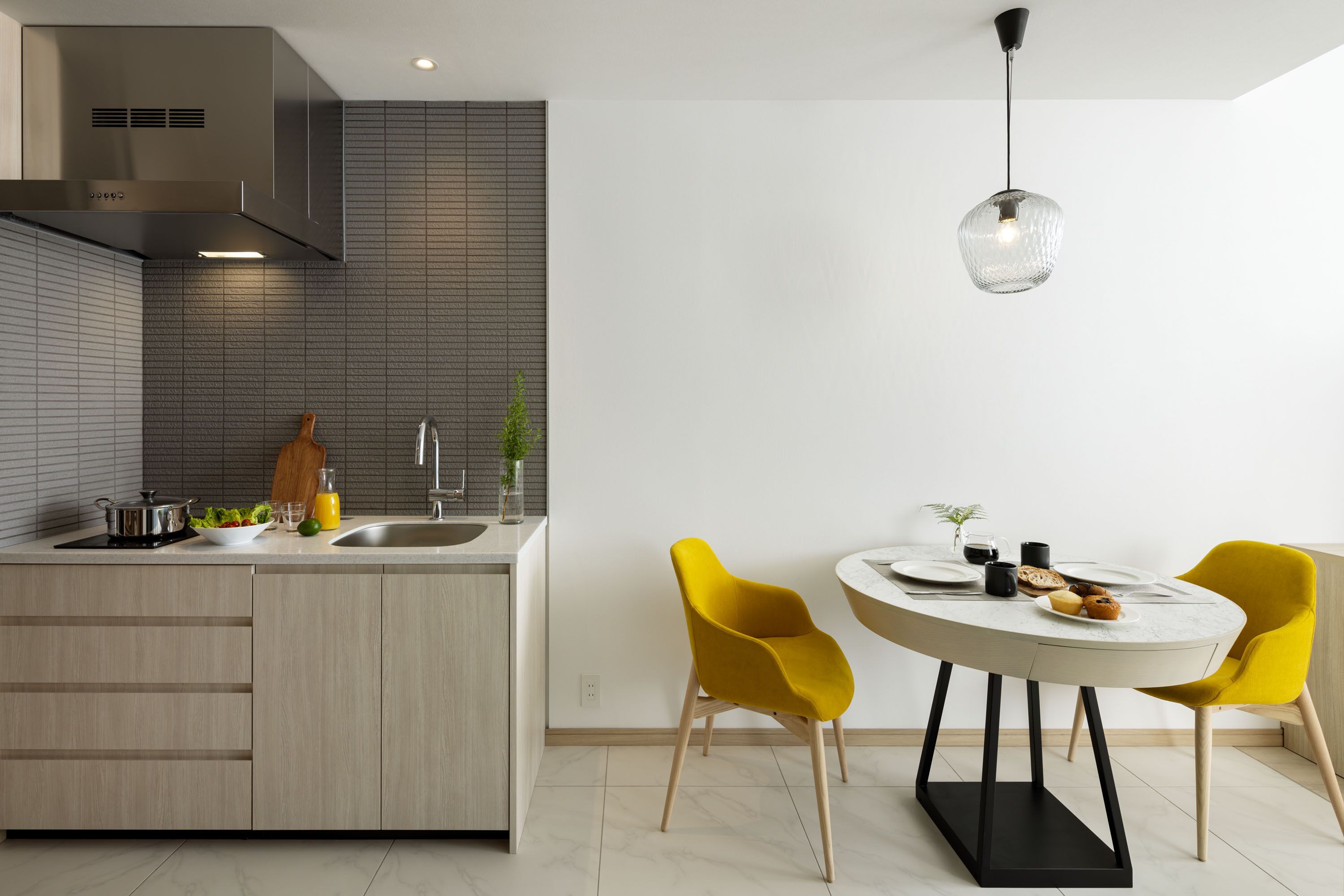 A modern kitchen with a built-in island, a dining area with yellow chairs, and a pendant light.